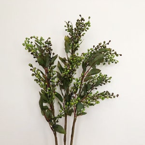 May include: A bunch of artificial green berry sprigs with small green berries and dark green leaves.