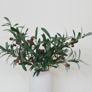 May include: A bouquet of artificial olive branches with green leaves and brown olives in a white ceramic vase.