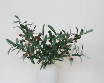 May include: A bouquet of artificial olive branches with green leaves and brown olives in a white ceramic vase.