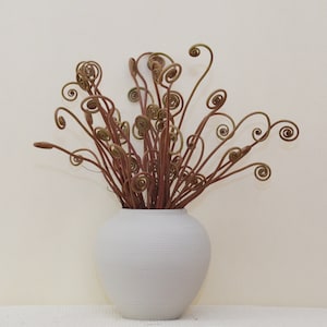 May include: A white ceramic vase with a textured surface holds a bouquet of dried fern fronds with curled tips.