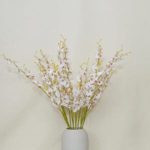 Puede incluir: Un ramo de flores blancas y rosas con tallos amarillos en un jarrón blanco. Las flores tienen pétalos delicados y están dispuestas para crear una exhibición completa y exuberante. El jarrón es de diseño simple y moderno.