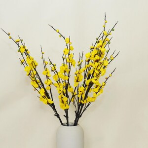 May include: A bouquet of yellow flowers with thin black stems arranged in a grey ceramic vase.