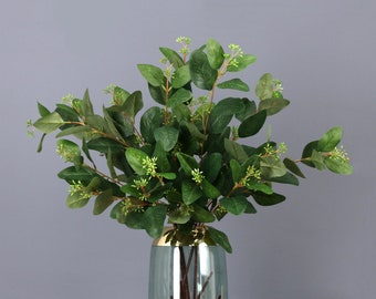 May include: A bouquet of artificial eucalyptus branches with green leaves and small white flowers in a clear glass vase.