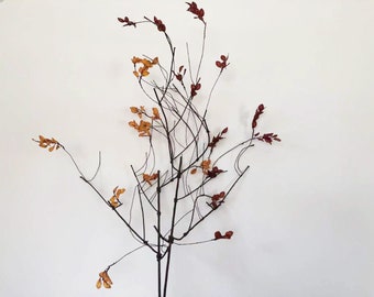 Peut inclure: Décoration murale en métal représentant une branche d'arbre stylisée. Les branches sont brun foncé, avec des touches de feuilles orange et rouges. L'œuvre est posée sur un fond blanc, idéale pour la décoration intérieure.