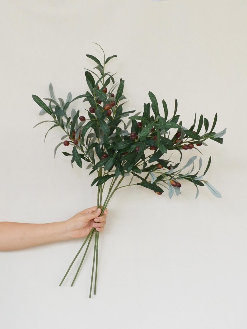 May include: A bouquet of artificial olive branches with green leaves and small, dark purple olives.