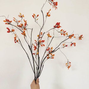 May include: A bouquet of artificial branches with small orange leaves. The branches are brown and have a natural, rustic look.