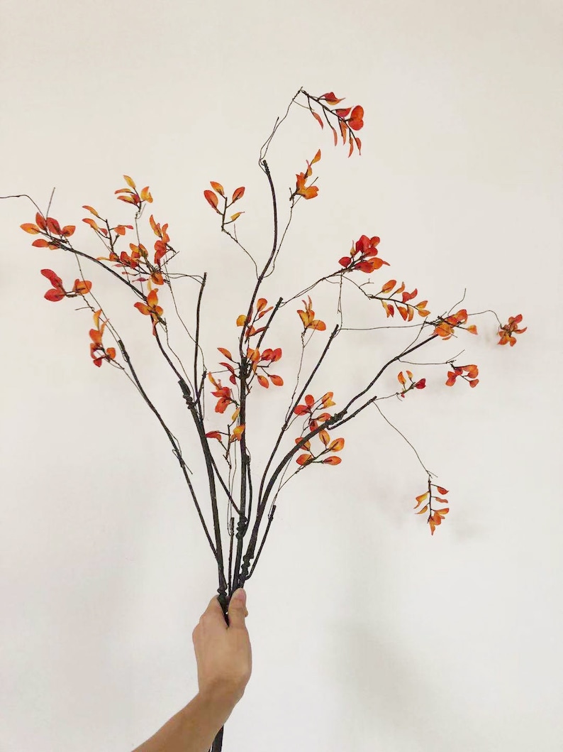 May include: A bouquet of artificial branches with small orange leaves. The branches are brown and have a natural, rustic look.