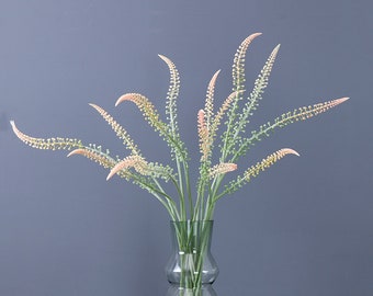 May include: A bouquet of artificial flowers in a clear glass vase. The flowers are a light pink color and have a delicate, feathery texture. The vase is a simple, elegant design.