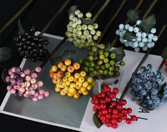 Puede incluir: Surtido de ramitas de bayas artificiales en varios colores, incluyendo morado, rojo, amarillo, verde, azul y negro. Las bayas están agrupadas en tallos con hojas verdes.