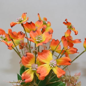 Puede incluir: Un ramo de flores artificiales con pétalos de color naranja y amarillo. Las flores tienen una apariencia delicada y en capas y están dispuestas en un racimo.
