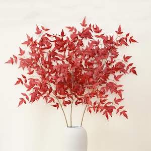 Puede incluir: Un ramo de hojas artificiales rojas en un jarrón blanco. Las hojas están dispuestas en cascada, creando una exhibición exuberante y vibrante.