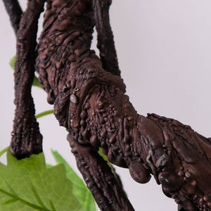 May include: Close-up of a brown, textured, artificial vine with a green leaf. The vine is made to look like a real vine with a rough, bark-like texture.