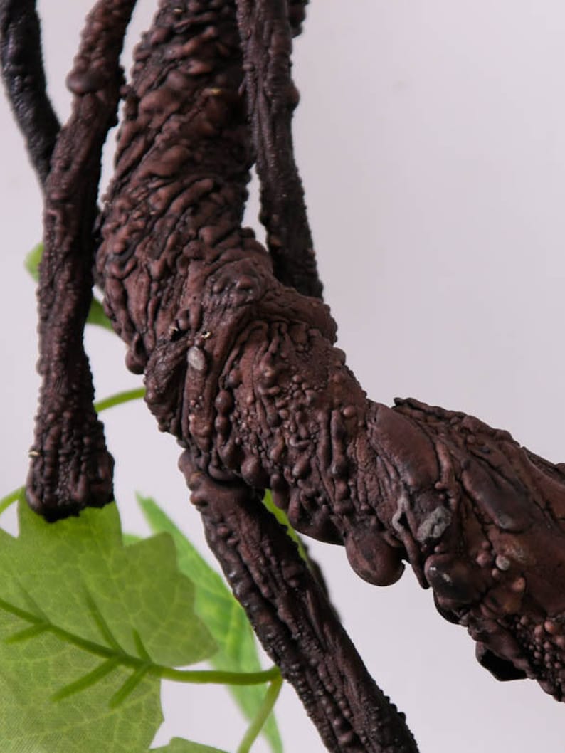May include: Close-up of a brown, textured, artificial vine with a green leaf. The vine is made to look like a real vine with a rough, bark-like texture.