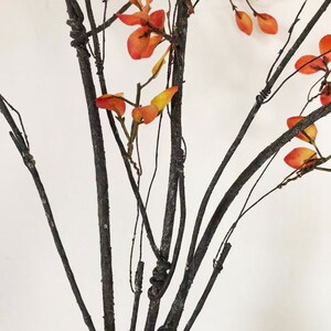 May include: A bouquet of artificial branches with dark brown stems and orange leaves.