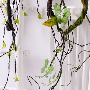 May include: Artificial vine with brown branches and green leaves. The vine is hanging from a white wooden ladder.