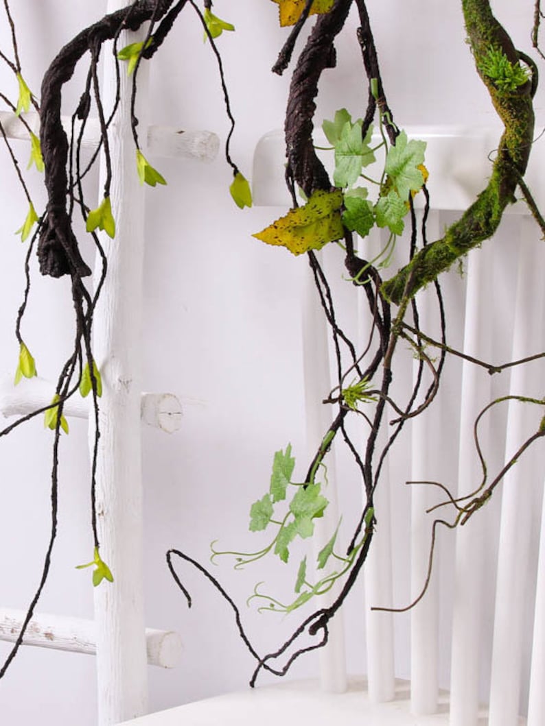 May include: Artificial vine with brown branches and green leaves. The vine is hanging from a white wooden ladder.