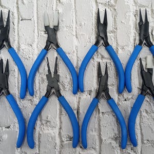 May include: Set of eight blue-handled jewelry pliers with black metal tips. The pliers are arranged in two rows of four, with the handles pointing outwards.