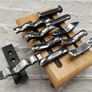 May include: A set of eight metal tools with different shaped heads, displayed on a wooden stand. The tools are polished and have a shiny finish.
