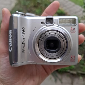 May include: Silver Canon PowerShot A560 digital camera. Features a 4x optical zoom lens and 7.1 megapixels. The camera has a built-in flash and the Canon logo is visible on the side.