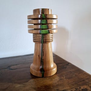 Può includere: Oggetto decorativo in legno chiaro fatto a mano. Presenta una serie di elementi circolari orizzontali e un'intarsio verticale in resina verde. La base è più larga, restringendosi verso l'alto.