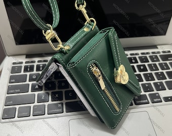 May include: A green leather wallet with a gold zipper and a gold heart-shaped charm. The wallet has a strap that can be used to carry it as a crossbody bag.