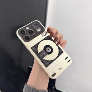 Peut inclure: Une coque de téléphone blanche avec un motif noir et blanc d'un tourne-disque et le texte "RICH-LUCKY-HAPPY" et "CLORYCREATION".