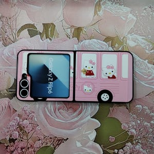 May include: A pink phone case with a Hello Kitty design. The case is a flip case with a window on the front that says "Galaxy Z Flip6".