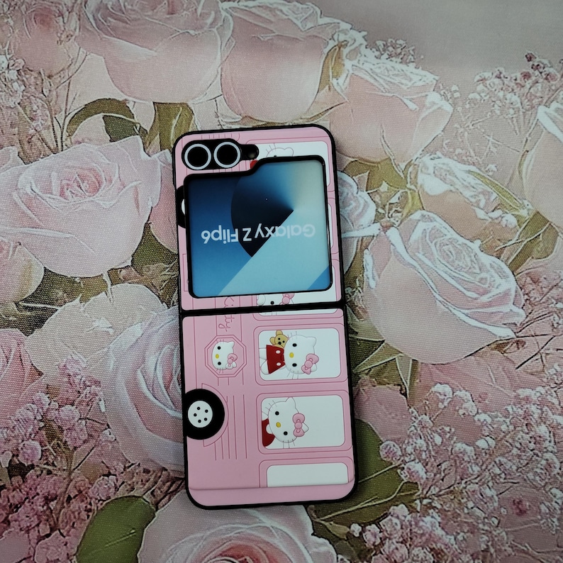 May include: A pink phone case with a Hello Kitty design. The case is designed to look like a bus with Hello Kitty characters on the windows. The phone case is for a Samsung Galaxy Z Flip 4.