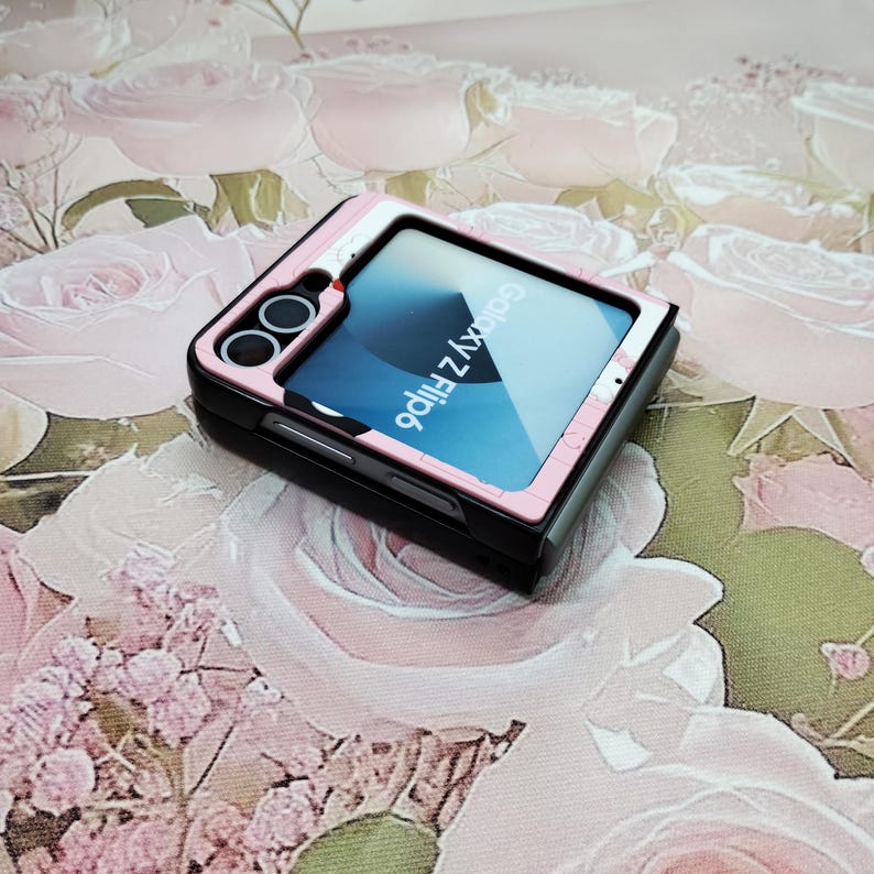 May include: A pink and black Galaxy Z Flip phone case with a clear back panel showing the phone's screen. The phone's screen displays the text "Galaxy Z Flip".