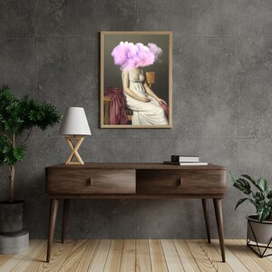 Pu&ograve; includere: Un dipinto incorniciato di una donna seduta su una sedia con una nuvola rosa che le copre la testa. La donna indossa un vestito bianco e siede su una sedia rossa. Il dipinto &egrave; posto contro un muro grigio con un tavolo di legno e una lampada di fronte ad esso.