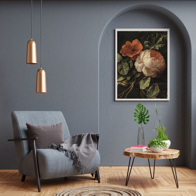 May include: A framed floral print with a white background featuring a bouquet of pink and orange roses with green leaves. The print is hanging on a gray wall above a gray armchair with a throw blanket and a small wooden table with a vase of green plants.