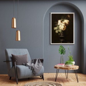 May include: A gray armchair with a throw blanket sits in a room with a wooden coffee table and a framed print of white roses in a vase. The room has a gray wall and a vaulted ceiling.