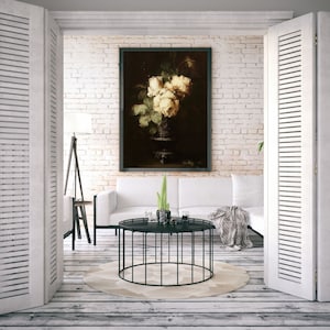 May include: A white framed painting of a bouquet of white roses in a vase, hanging on a white brick wall in a living room with a white couch and a black coffee table.