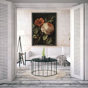 May include: A white couch with throw pillows sits in front of a white brick wall. A black framed painting of a still life with orange and white flowers hangs on the wall. A black metal coffee table with a round top sits in front of the couch. A potted plant sits on the coffee table.