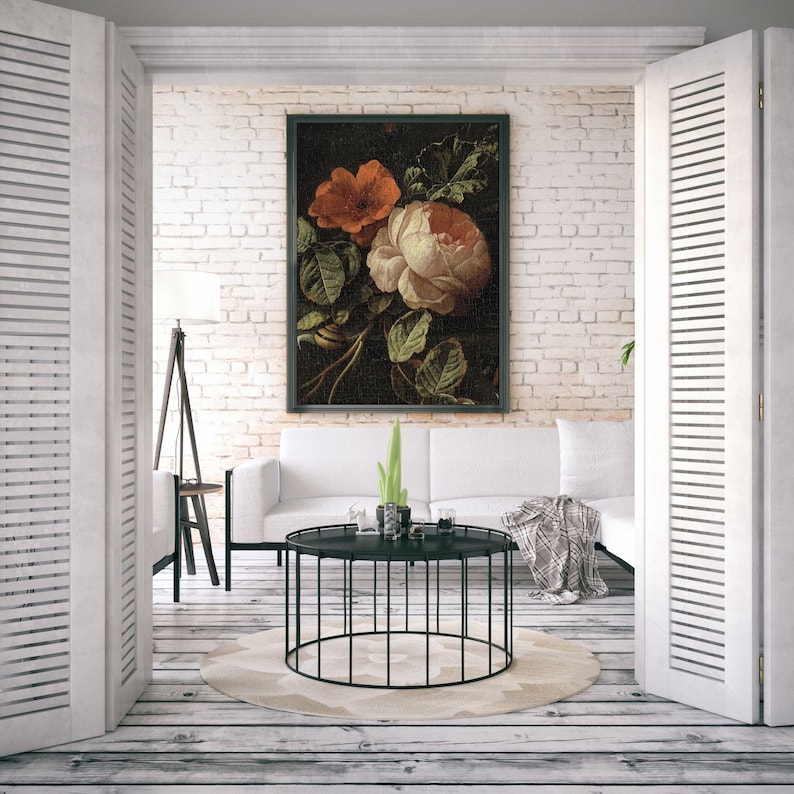 May include: A white couch with throw pillows sits in front of a white brick wall. A black framed painting of a still life with orange and white flowers hangs on the wall. A black metal coffee table with a round top sits in front of the couch. A potted plant sits on the coffee table.