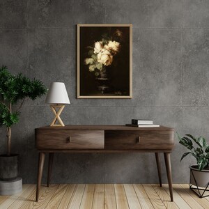 May include: A framed print of a still life painting featuring a bouquet of white roses in a dark vase against a dark background.
