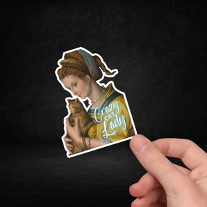May include: A sticker featuring a Renaissance-style painting of a woman holding a cat. The woman is wearing a blue and gold dress and a pearl necklace. The text "Crazy Cat Lady" is written in a whimsical font.