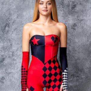 May include: A strapless jumpsuit in a striking red, black, and white color scheme. The bodice features a star and diamond pattern, with matching arm sleeves. The lower half of the jumpsuit has a diamond pattern.