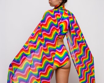 May include: A rainbow-coloured swimsuit with a wavy pattern. The swimsuit has a high-waisted bottom and a halter top. The swimsuit is paired with a matching rainbow-coloured cape with a wavy pattern.