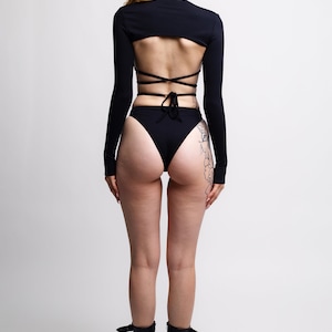 May include: Black long-sleeved crop top with a criss-cross back design and matching high-waisted bikini bottoms. The model is wearing black platform boots.