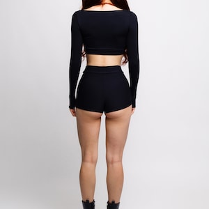 May include: A woman wearing a black long-sleeved crop top and black shorts. She is wearing black platform boots.