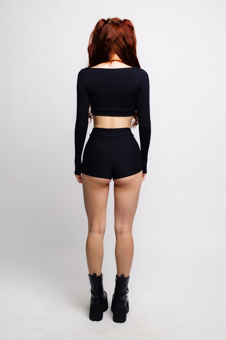 May include: A woman wearing a black long-sleeved crop top and black shorts. She is wearing black platform boots.