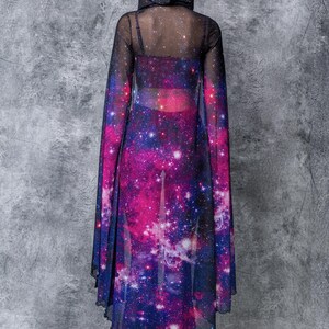 May include: A sheer black hooded top with a galaxy print. The top is long-sleeved and has a flowing, cape-like design. The print features a dark blue background with pink, purple, and white stars.