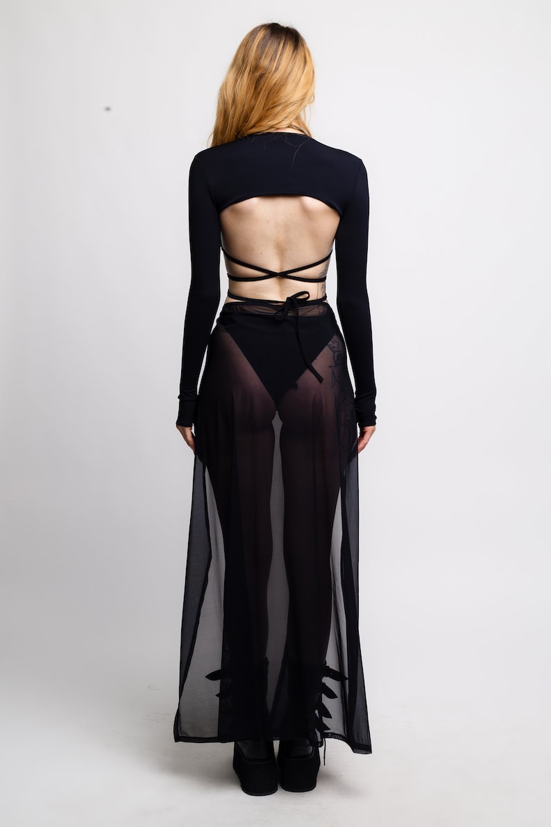 May include: A black long-sleeved crop top with a tie-up back detail and a sheer black maxi skirt.