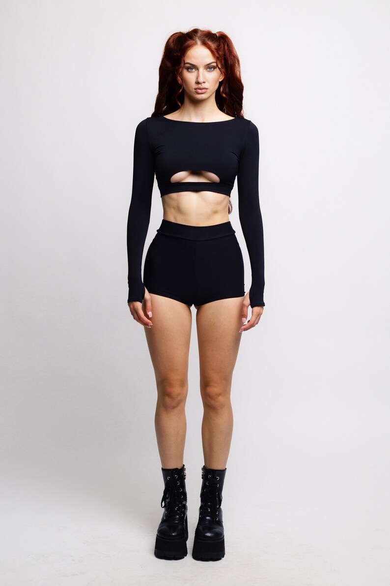 May include: A woman wearing a black long-sleeved crop top with a cut-out detail and black high-waisted shorts. She is wearing black platform boots.
