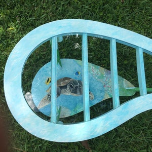 May include: A blue, wave-shaped table with a glass top. The glass top features a painted design of a sea turtle swimming in the ocean with coral and fish.