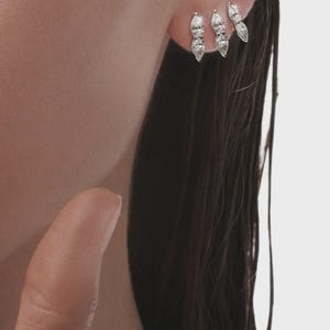 Könnte beinhalten: Drei silberne Ohrringe mit klaren, tropfenförmigen Steinen sind an einem Ohr zu sehen. Die Ohrringe sind in einer Reihe angeordnet, wobei die Steine das Licht einfangen. Der Schmuck ist schlicht und elegant, passend für Alltag oder besondere Anlässe.
