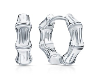 May include: A pair of silver hoop earrings featuring a textured bamboo-inspired design. The earrings have a polished metallic finish with segmented nodes that mimic the appearance of bamboo stalks, complete with a hinged closure mechanism.
