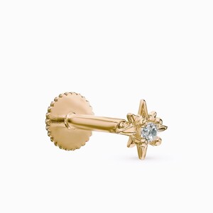 May include: Gold star-shaped stud earring with a small clear gemstone in the center. The earring has a threaded back.