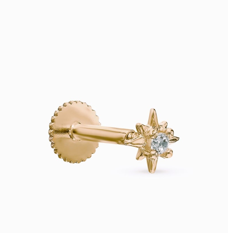 May include: Gold star-shaped stud earring with a small clear gemstone in the center. The earring has a threaded back.